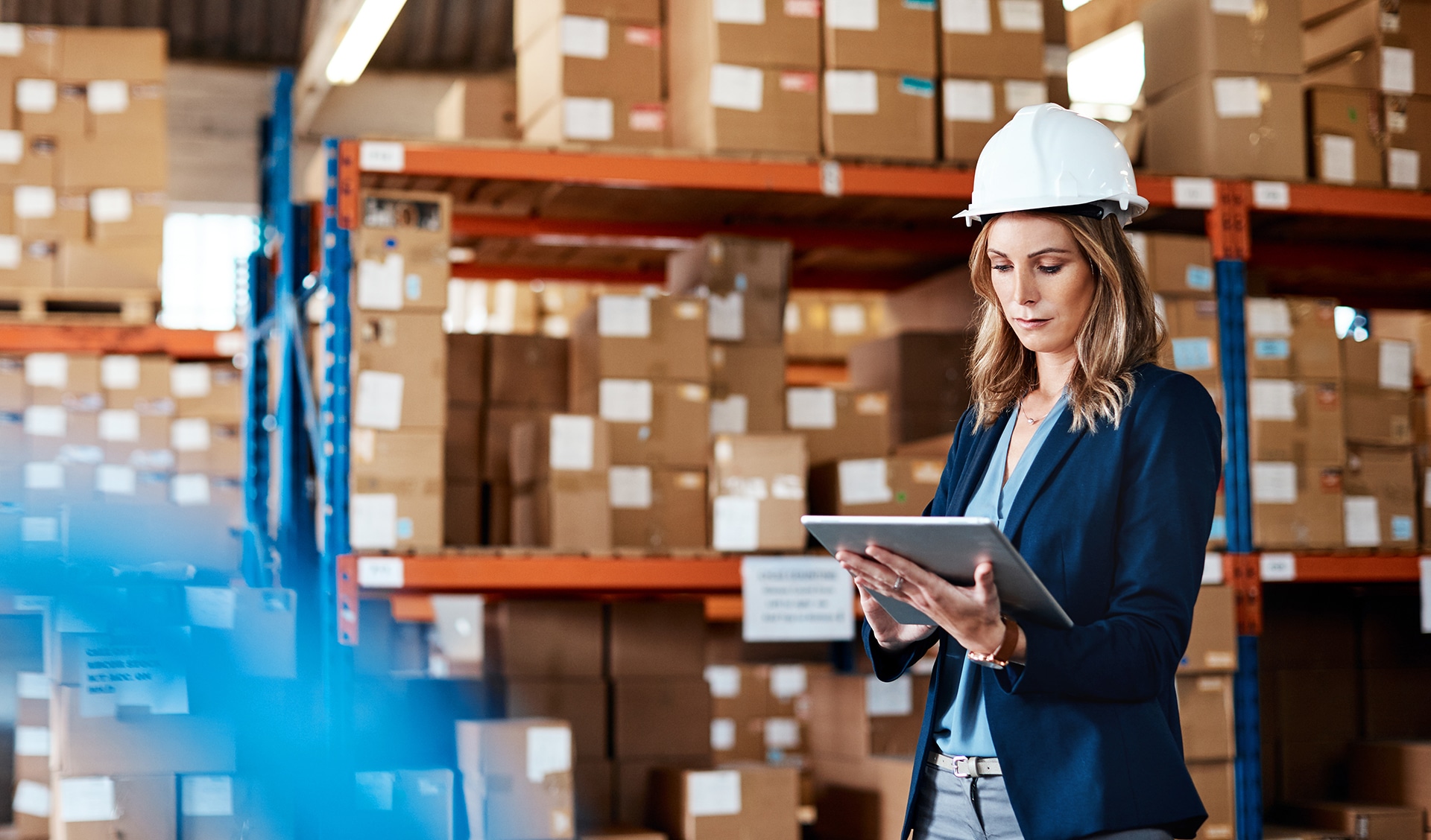 Woman wearing hard hat looking at tablet computer in warehouse